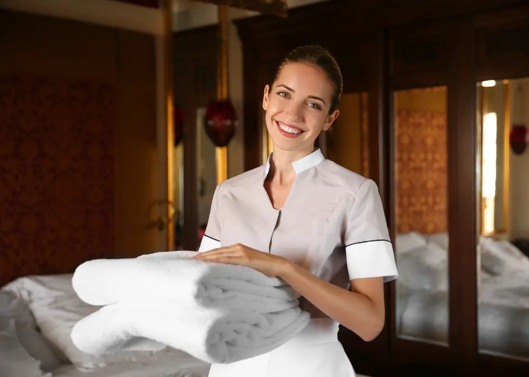 Woman in a hotel room holding folded towels with a warm ambiance