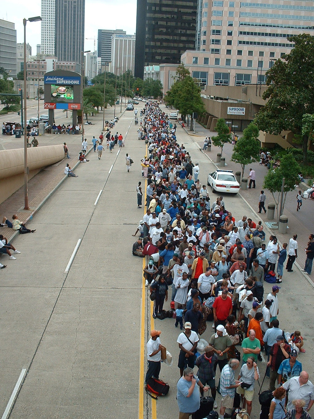 Large crowd of evacuees waiting for disaster relief assistance outside a mass care shelter, illustrating the scale of emergency response operations and the need for bulk humanitarian supplies.