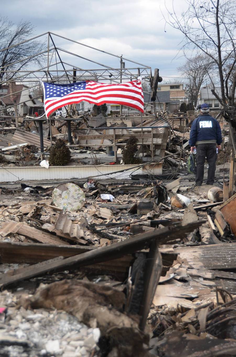 FEMA official surveying disaster debris with an American flag in the background, symbolizing national resilience and federal emergency recovery operations.
