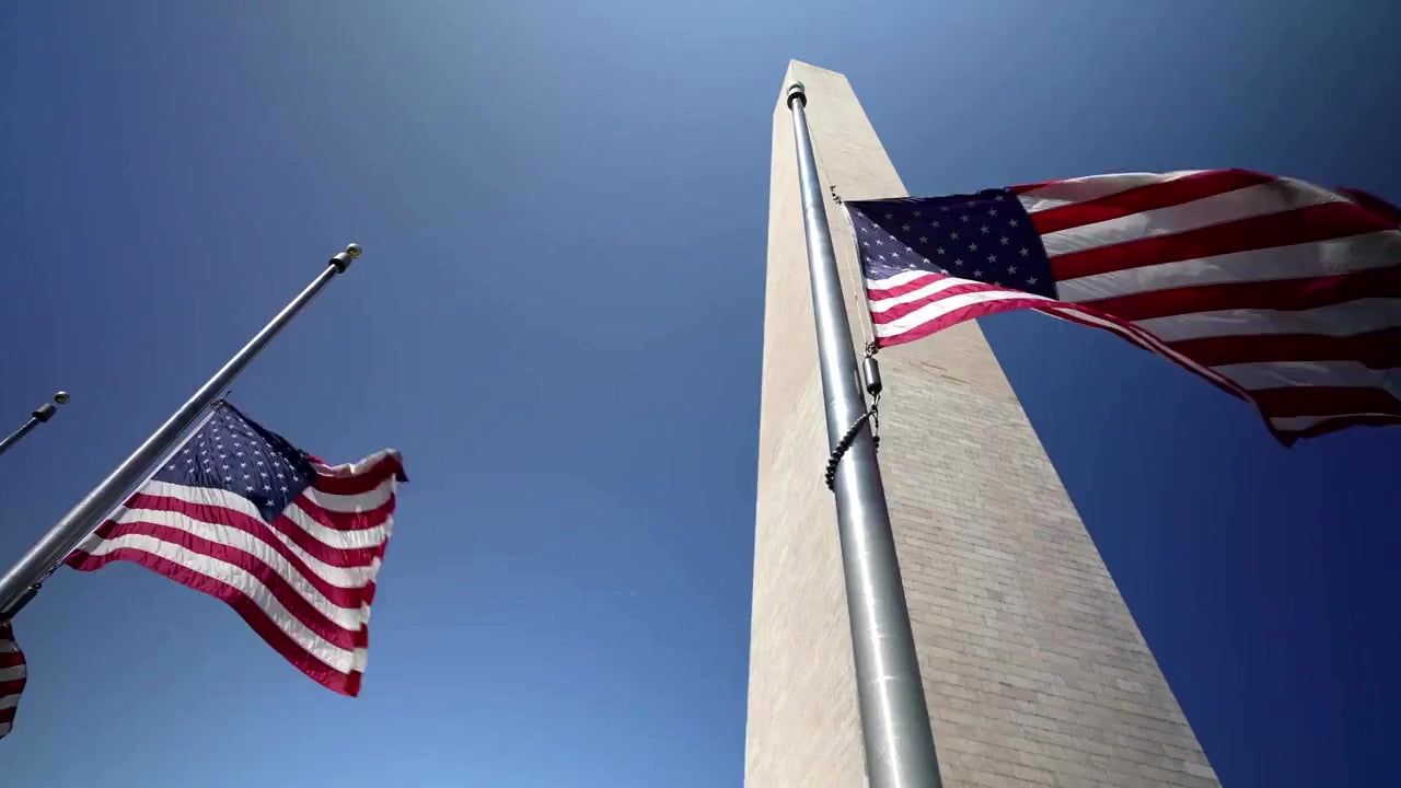 Load video: Panoramic video footage of the Washington Monument obelisk surrounded by waving US flags, symbolizing American heritage and a commitment to domestic supply chains for government contracting.